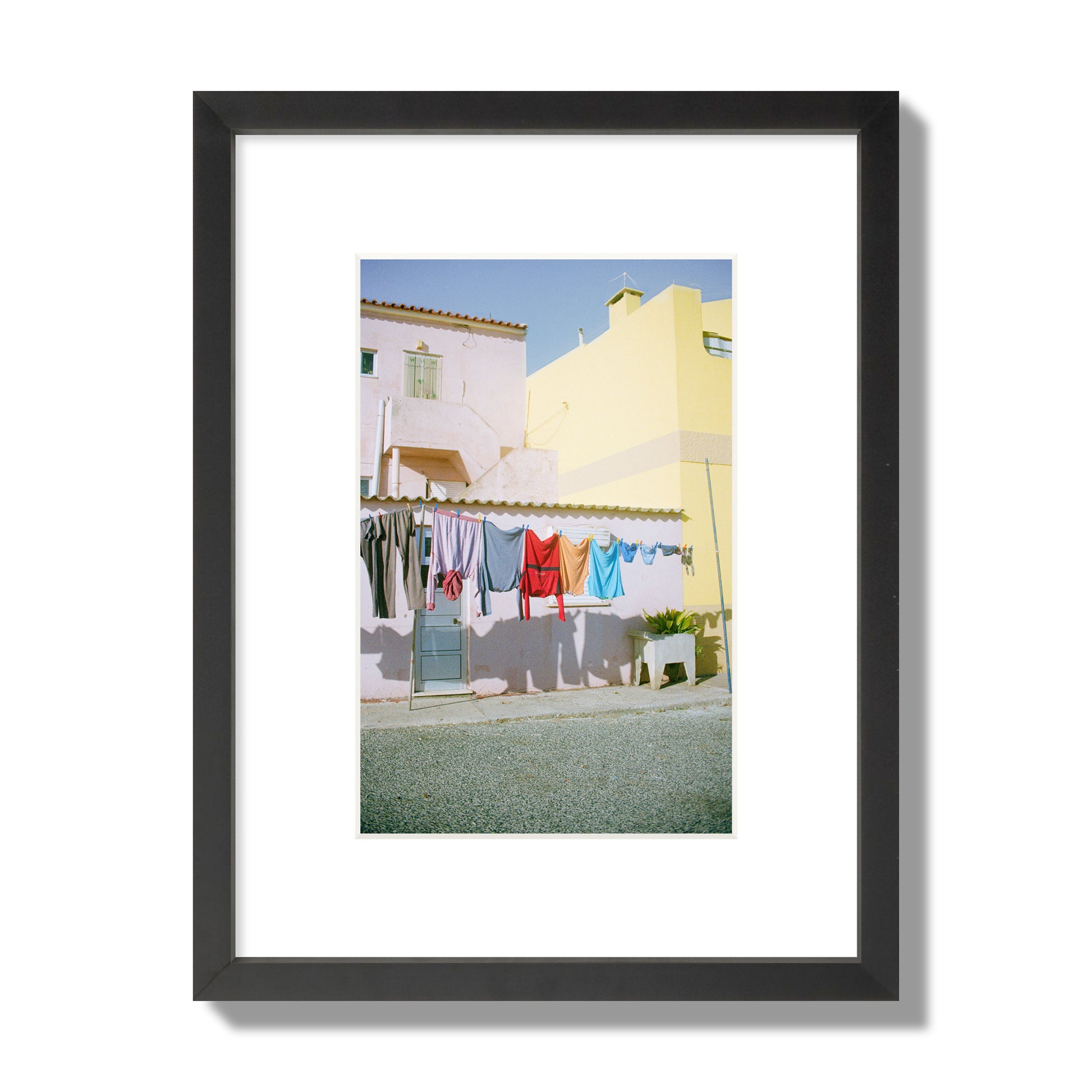 Fine art street photograph of a colorful outdoor scene in Portugal with clothes hanging on a line, archival pigment print, small size, black frame.