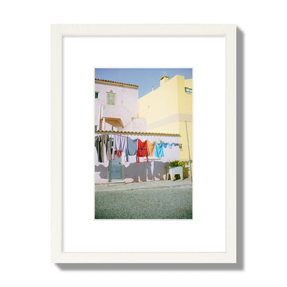Fine art street photograph of a colorful outdoor scene in Portugal with clothes hanging on a line, archival pigment print, small size, white frame.