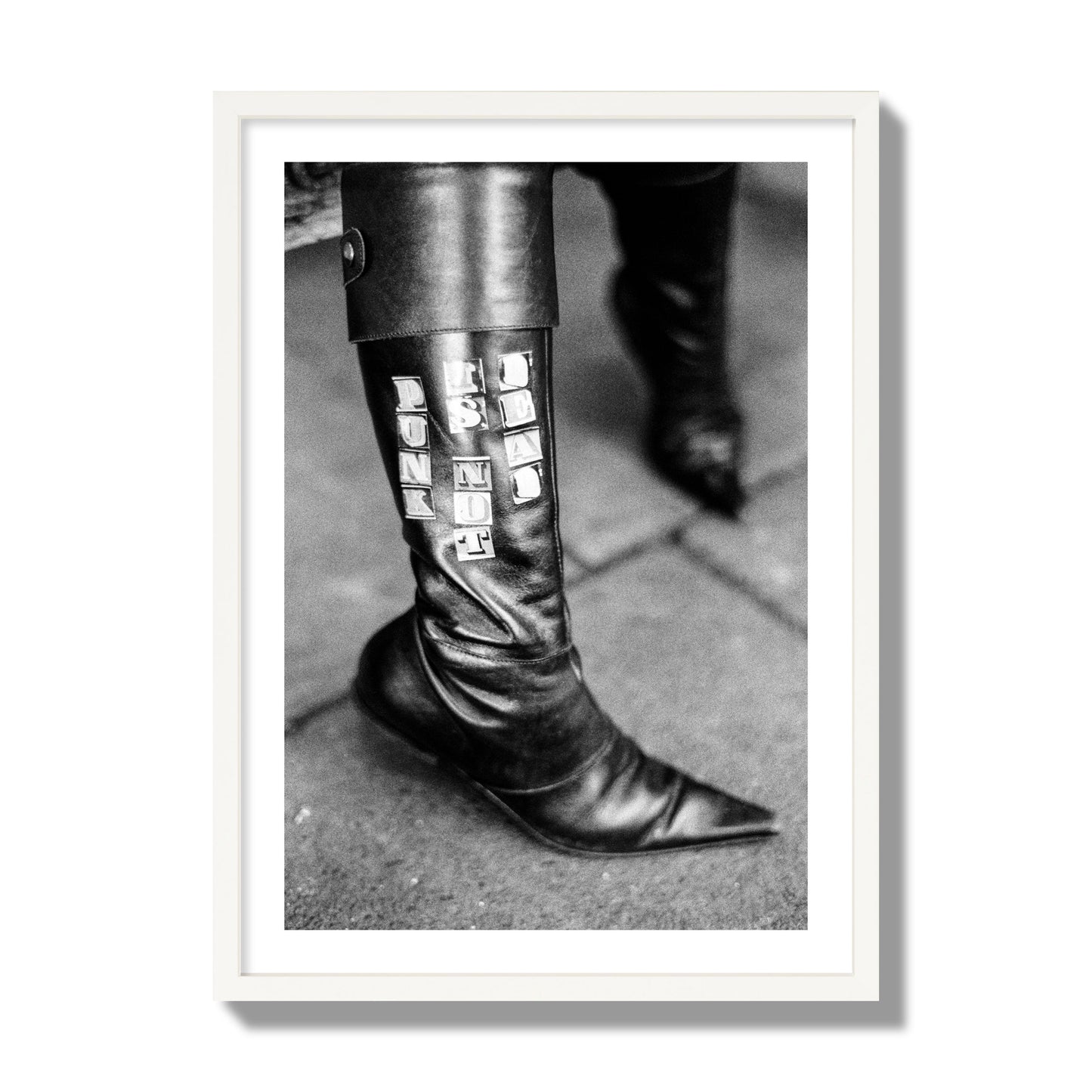 Fine art black and white photo of a woman's black leather boot with the words Punk is Not Dead, archival pigment print, giant size, white frame.