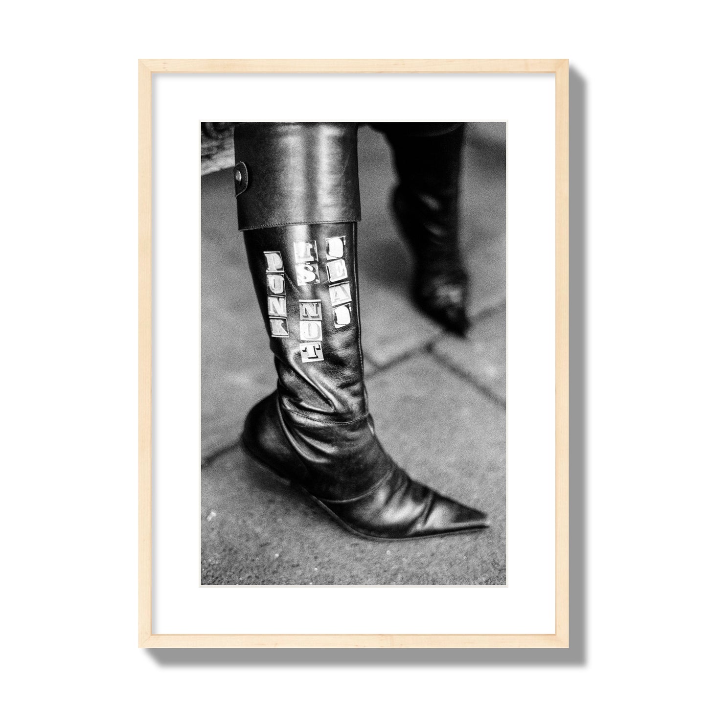 Fine art black and white photo of a woman's black leather boot with the words Punk is Not Dead, archival pigment print, large size, natural wood frame.