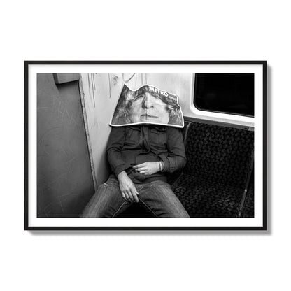 Fine art photograph of a man asleep on the subway with a newspaper covering their face, archival pigment print, collector size, black frame.