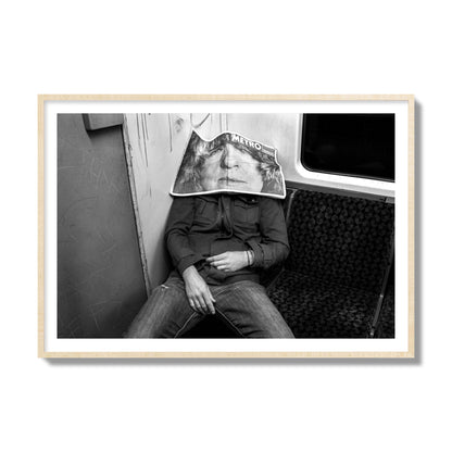 Fine art photograph of a man asleep on the subway with a newspaper covering their face, archival pigment print, collector size, natural wood frame.