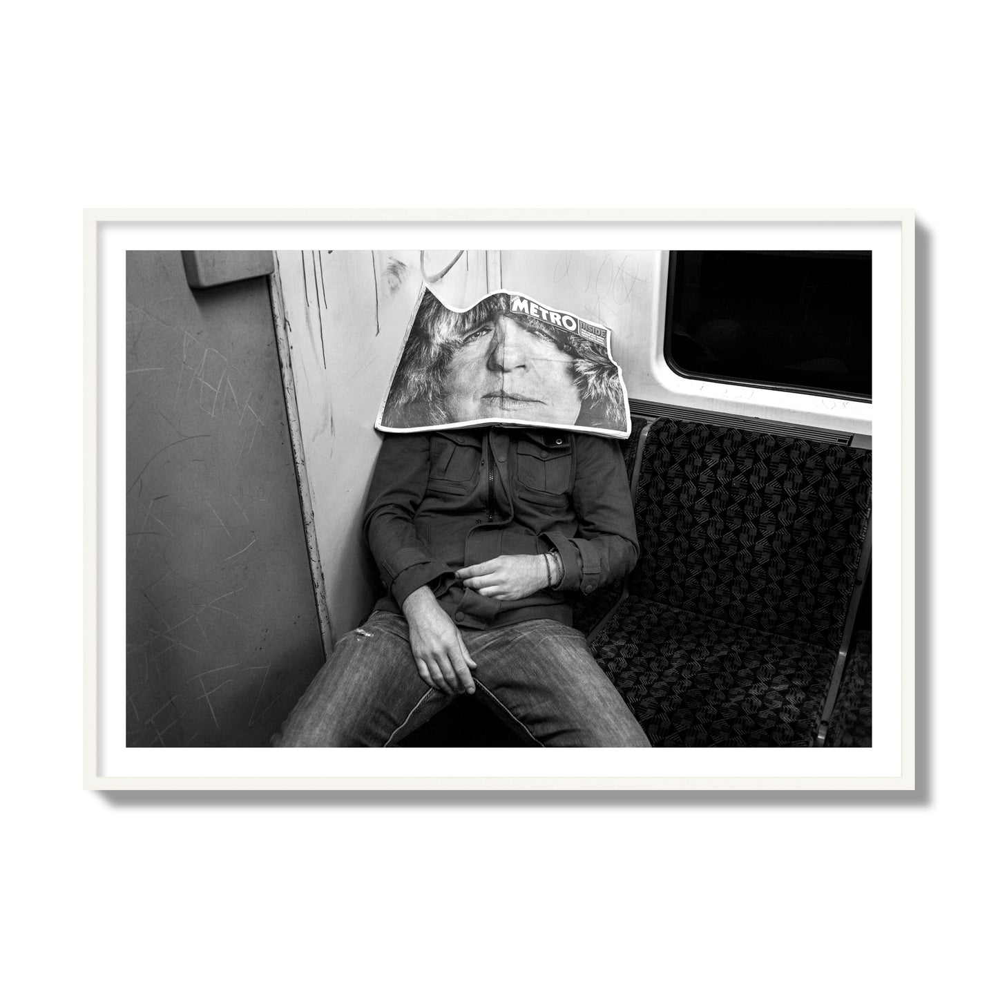 Fine art photograph of a man asleep on the subway with a newspaper covering their face, archival pigment print, collector size, white frame.