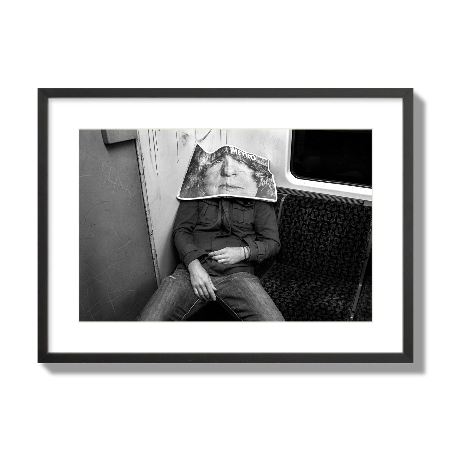 Fine art photograph of a man asleep on the subway with a newspaper covering their face, archival pigment print, large size, black frame.