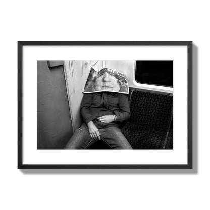 Fine art photograph of a man asleep on the subway with a newspaper covering their face, archival pigment print, large size, black frame.
