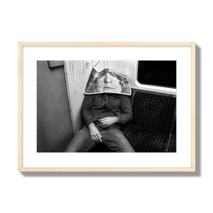 Fine art photograph of a man asleep on the subway with a newspaper covering their face, archival pigment print, large size, natural wood frame.
