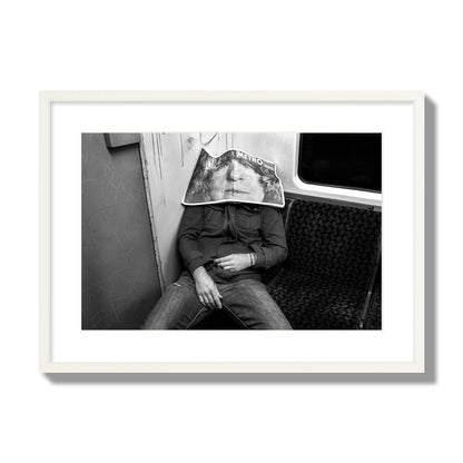 Fine art photograph of a man asleep on the subway with a newspaper covering their face, archival pigment print, large size, white frame.