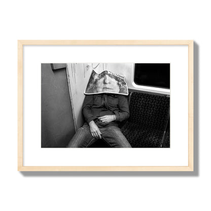 Fine art photograph of a man asleep on the subway with a newspaper covering their face, archival pigment print, medium size, natural wood frame.