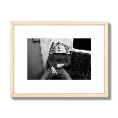 Fine art photograph of a man asleep on the subway with a newspaper covering their face, archival pigment print, small size, natural wood frame.