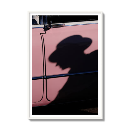 Fine art photograph of a man's shadow cast on a pink retro car, archival pigment print, gallery size, white frame.