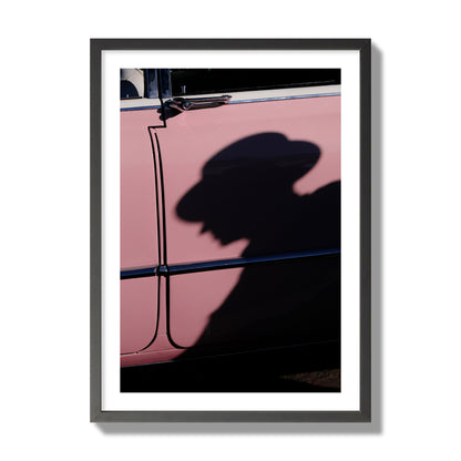 Fine art photograph of a man's shadow cast on a pink retro car, archival pigment print, giant size, black frame.