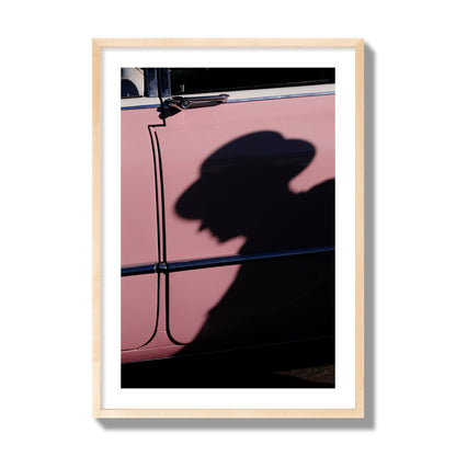 Fine art photograph of a man's shadow cast on a pink retro car, archival pigment print, giant size, natural wood frame.