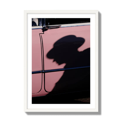 Fine art photograph of a man's shadow cast on a pink retro car, archival pigment print, giant size, white frame.