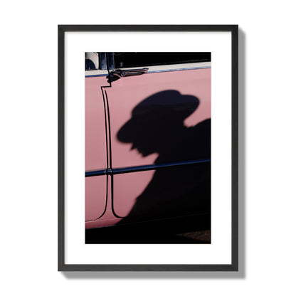 Fine art photograph of a man's shadow cast on a pink retro car, archival pigment print, large size, black frame.