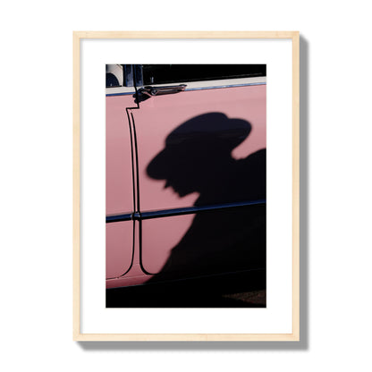 Fine art photograph of a man's shadow cast on a pink retro car, archival pigment print, large size, natural wood frame.