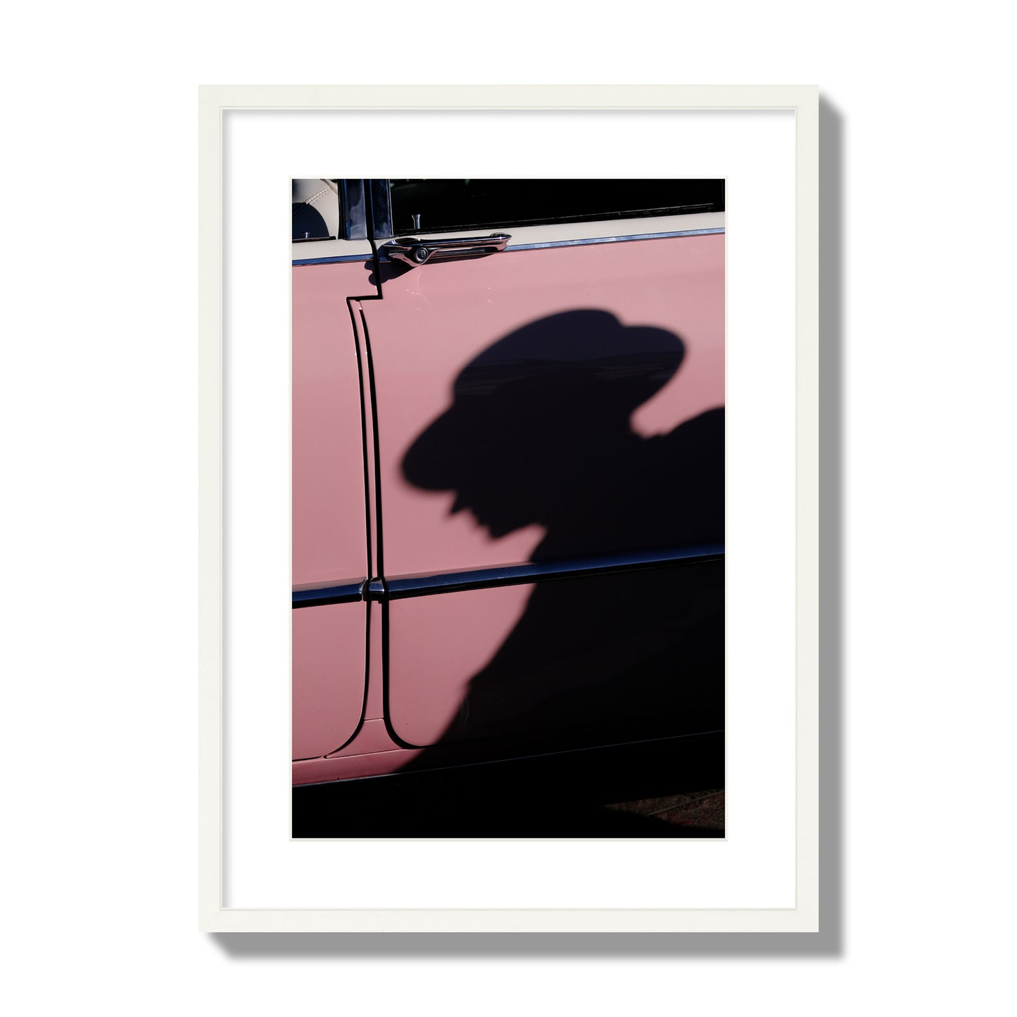 Fine art photograph of a man's shadow cast on a pink retro car, archival pigment print, large size, white frame.