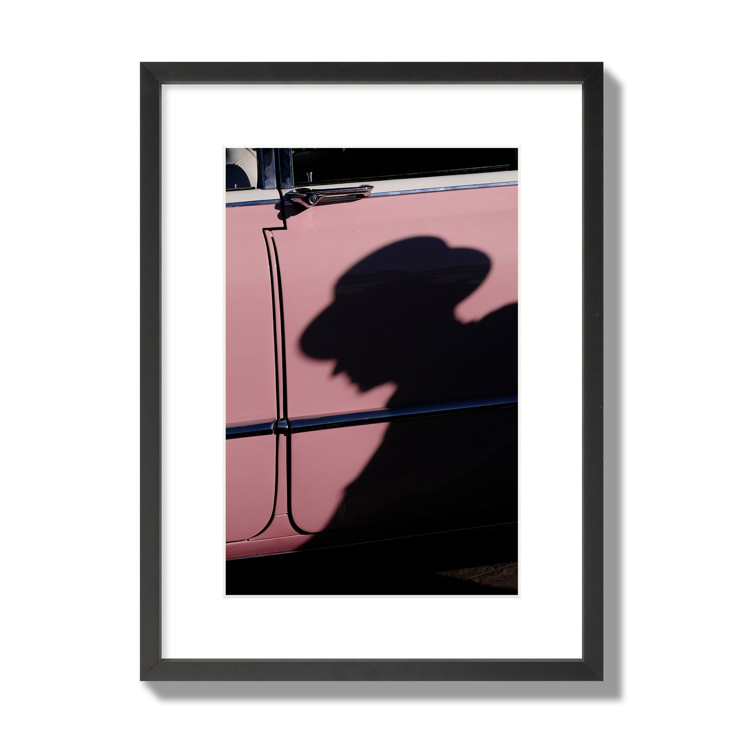 Fine art photograph of a man's shadow cast on a pink retro car, archival pigment print, medium size, black frame.