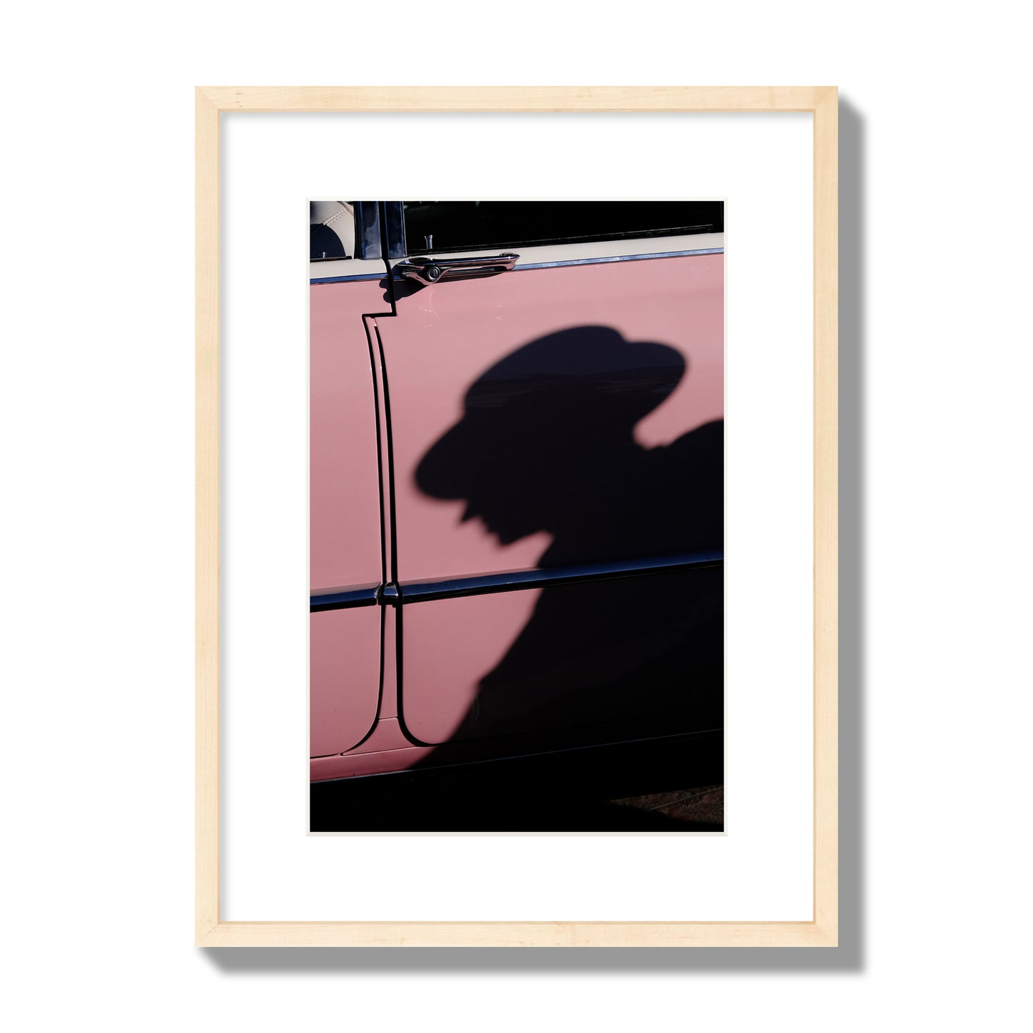 Fine art photograph of a man's shadow cast on a pink retro car, archival pigment print, medium size, natural wood frame.