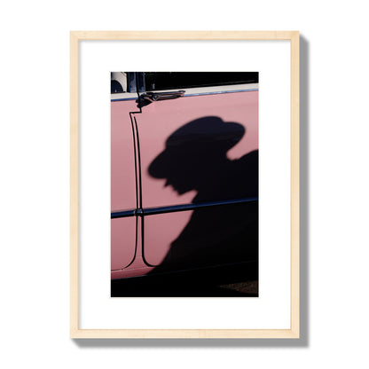 Fine art photograph of a man's shadow cast on a pink retro car, archival pigment print, medium size, natural wood frame.