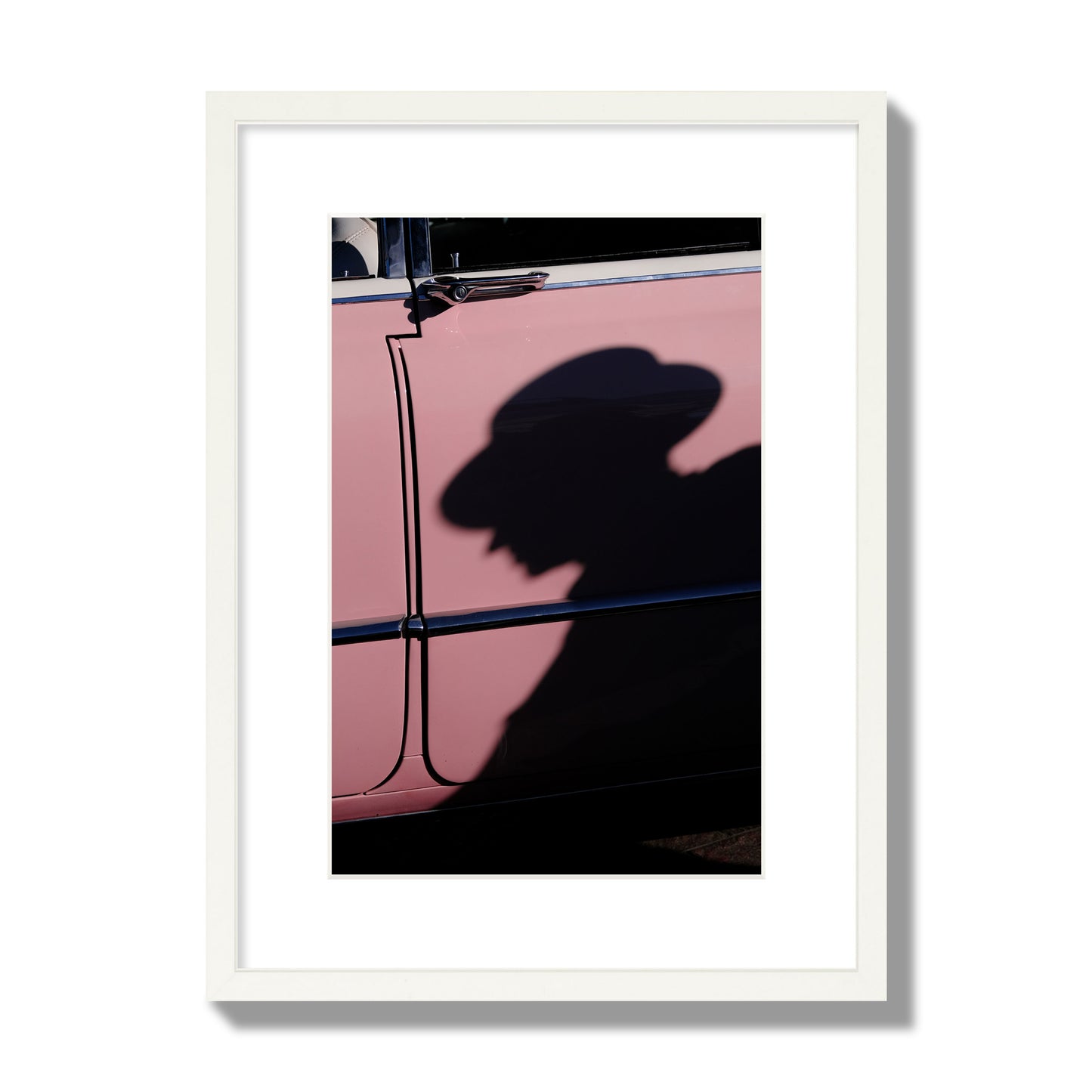 Fine art photograph of a man's shadow cast on a pink retro car, archival pigment print, medium size, white frame.