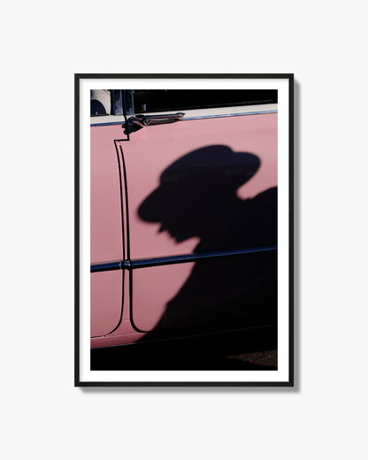 Fine art photograph of a man's shadow cast on a pink retro car, archival pigment print, black frame.