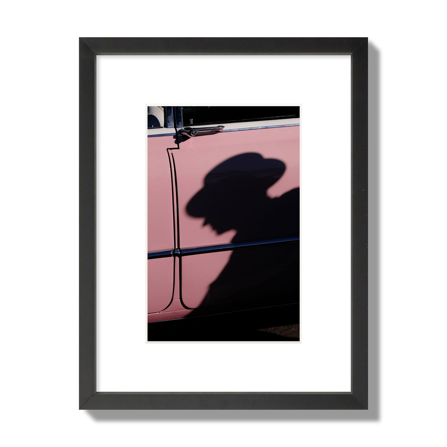 Fine art photograph of a man's shadow cast on a pink retro car, archival pigment print, small size, black frame.