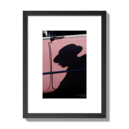 Fine art photograph of a man's shadow cast on a pink retro car, archival pigment print, small size, black frame.