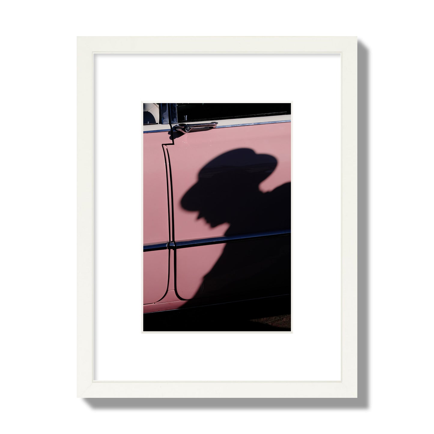 Fine art photograph of a man's shadow cast on a pink retro car, archival pigment print, small size, white frame.