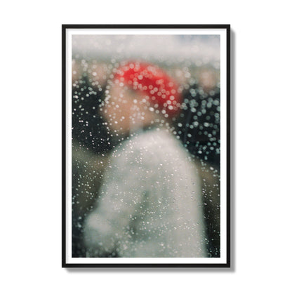 Fine art photograph of a woman with a red hat through raindrops on a window, archival pigment print, gallery size, black frame.