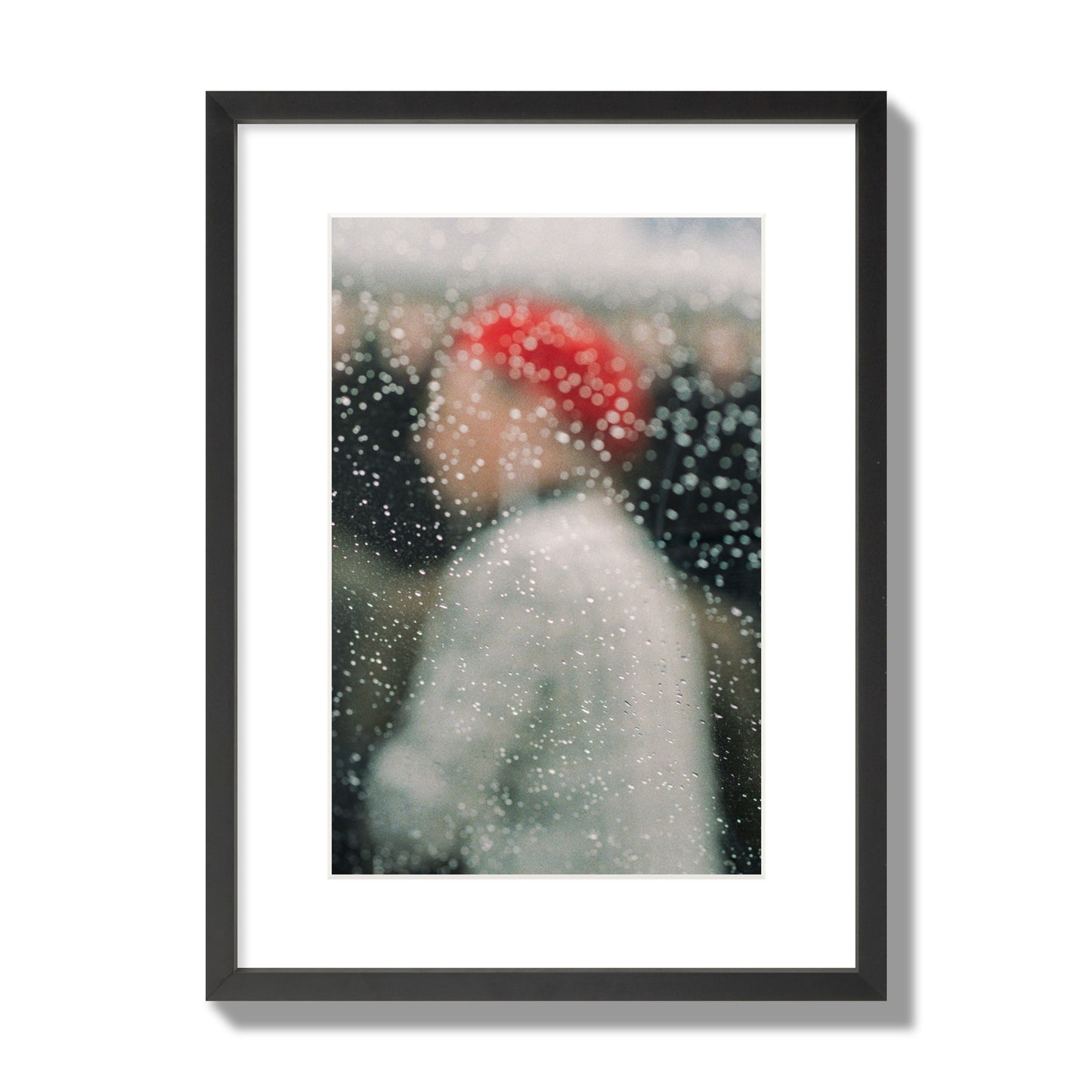 Fine art photograph of a woman with a red hat through raindrops on a window, archival pigment print, medium size, black frame.