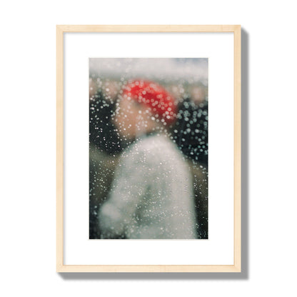 Fine art photograph of a woman with a red hat through raindrops on a window, archival pigment print, medium size, natural wood frame.