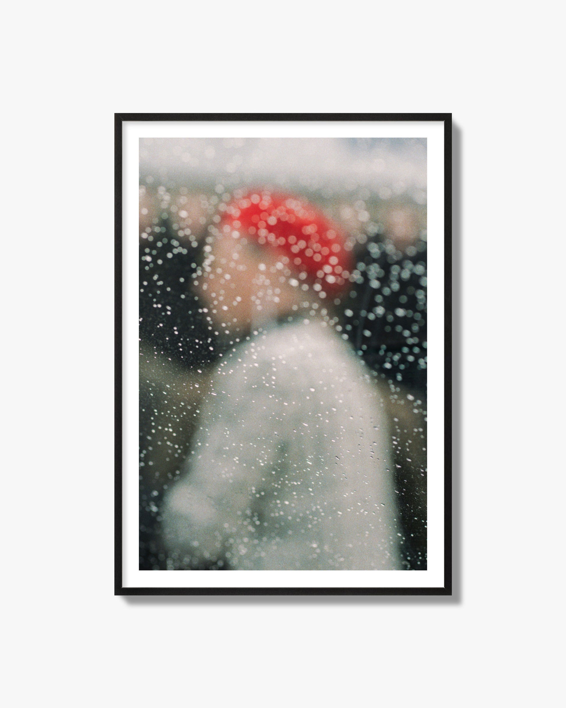 Fine art photograph of a woman with a red hat through raindrops on a window, archival pigment print, black frame.