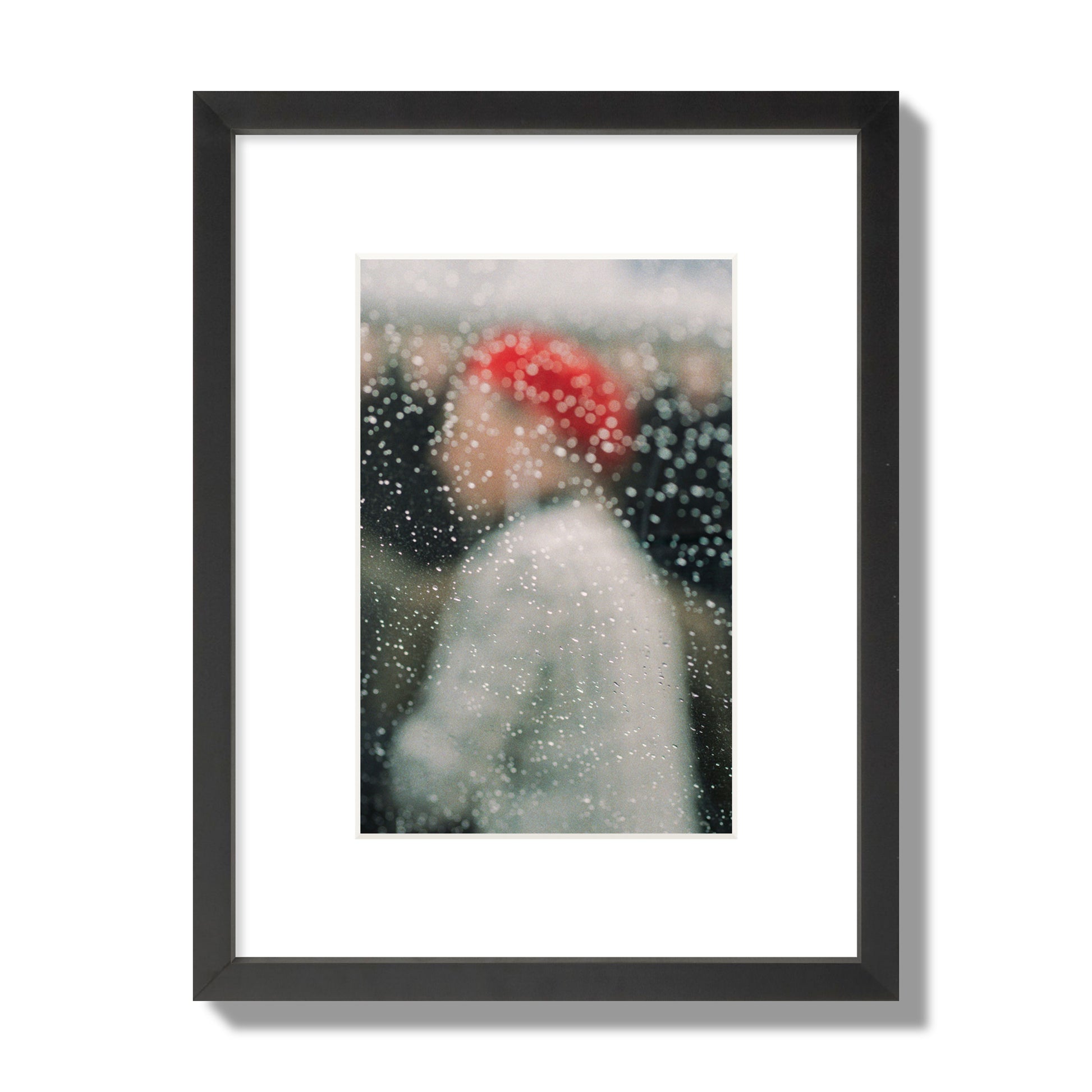 Fine art photograph of a woman with a red hat through raindrops on a window, archival pigment print, small size, black frame.