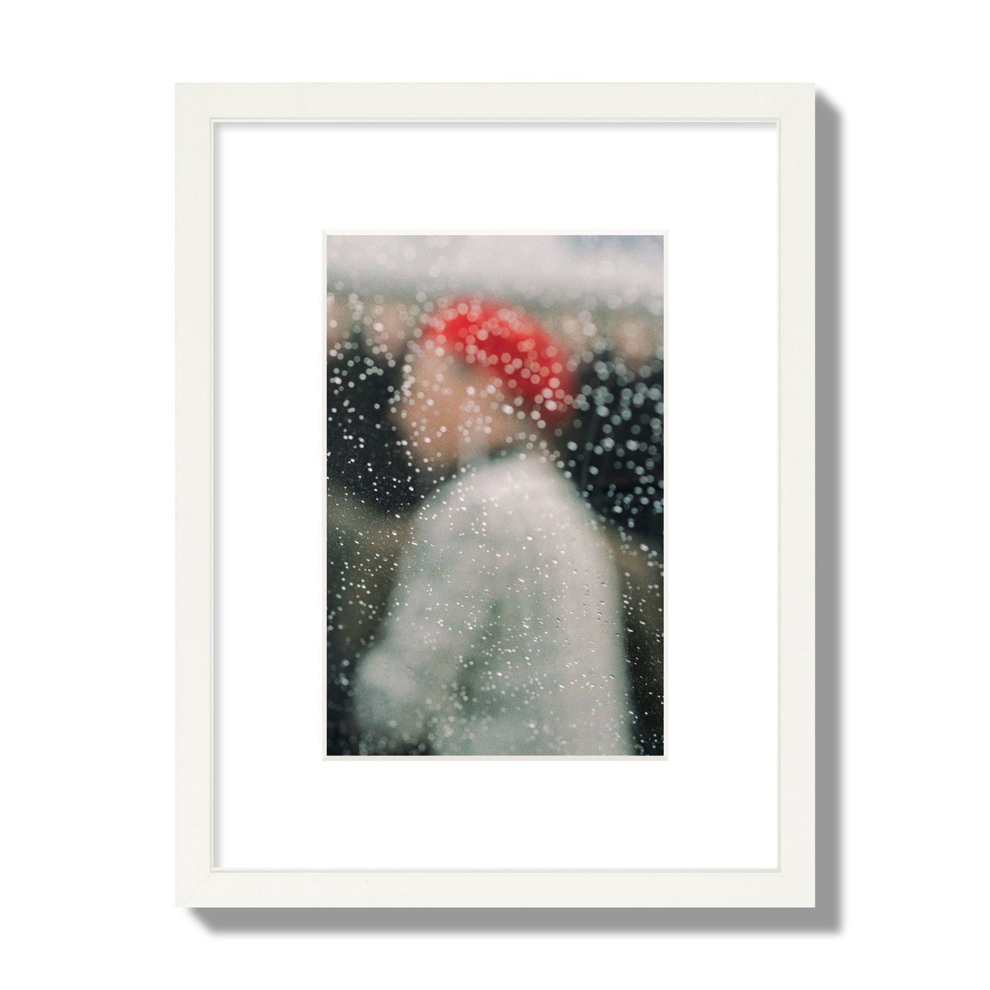 Fine art photograph of a woman with a red hat through raindrops on a window, archival pigment print, small size, white frame.