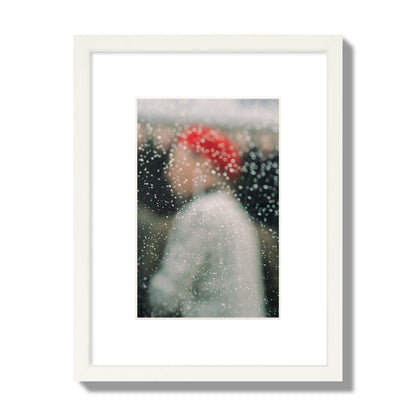 Fine art photograph of a woman with a red hat through raindrops on a window, archival pigment print, small size, white frame.