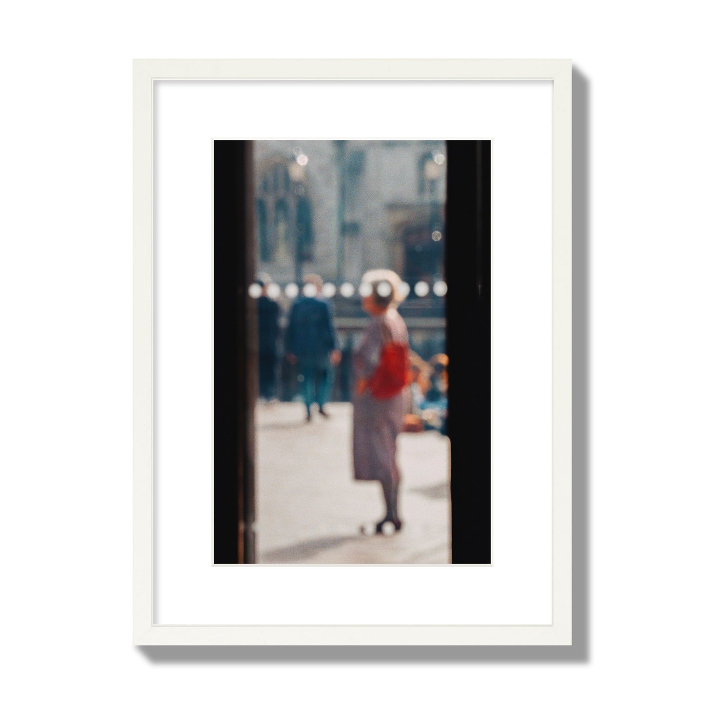 Fine art photograph of a blurred street scene with people and a storefront, archival pigment print, medium size, white frame.