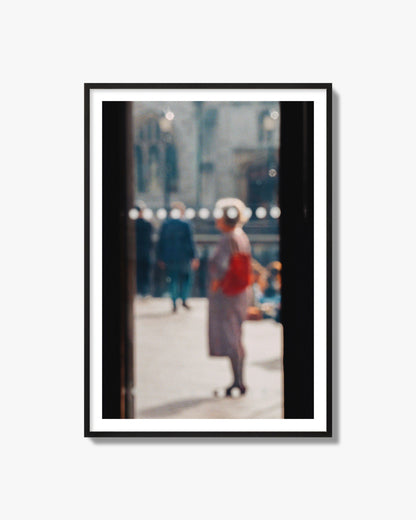 Fine art photograph of a blurred street scene with people and a storefront, archival pigment print, black frame.