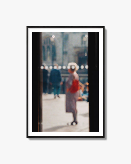 Fine art photograph of a blurred street scene with people and a storefront, archival pigment print, black frame.