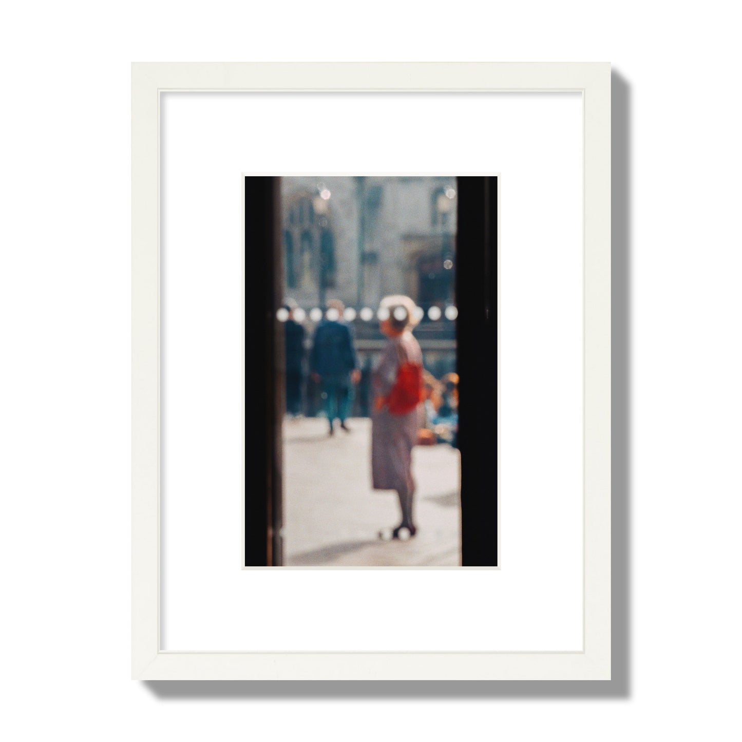 Fine art photograph of a blurred street scene with people and a storefront, archival pigment print, small size, white frame.