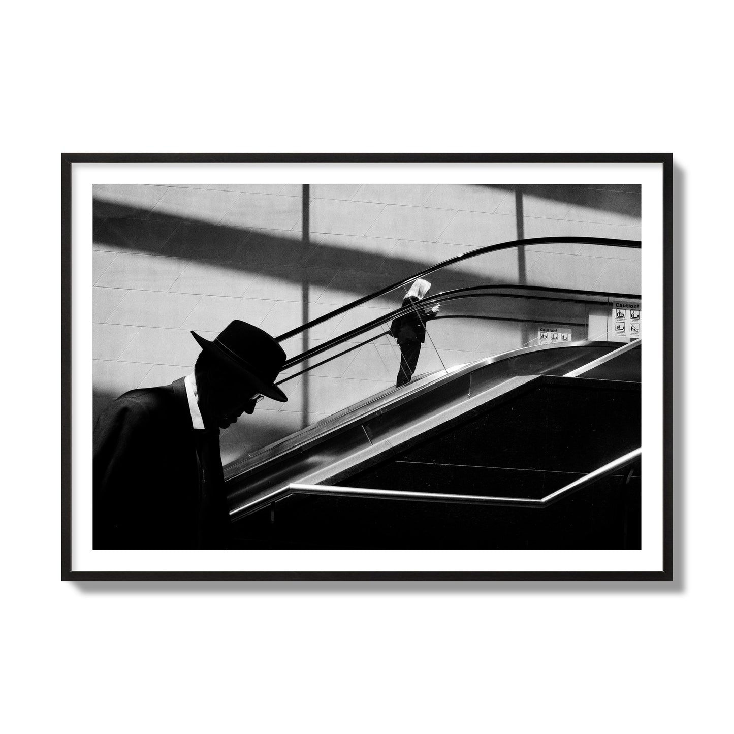 Fine art black and white street photograph of a man ascending an escalator. Archival pigment print, collector size, black frame.