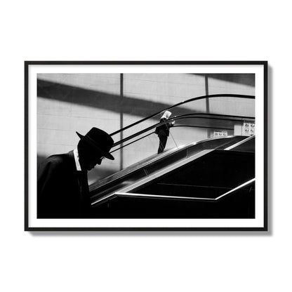 Fine art black and white street photograph of a man ascending an escalator. Archival pigment print, collector size, black frame.