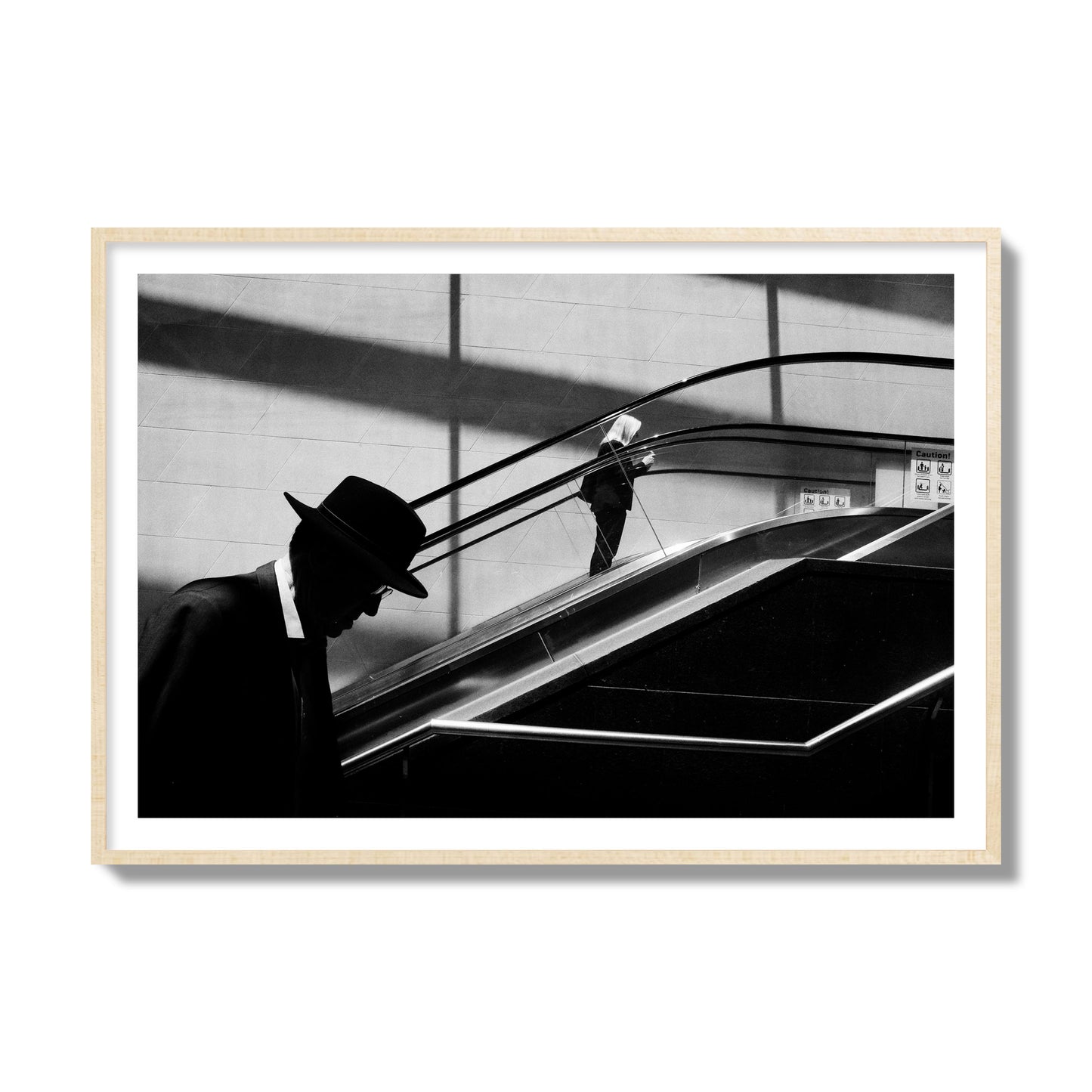 Fine art black and white street photograph of a man ascending an escalator. Archival pigment print, collector size, natural wood frame.