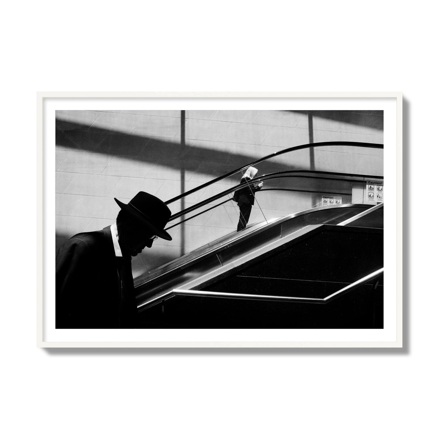 Fine art black and white street photograph of a man ascending an escalator. Archival pigment print, collector size, white frame.