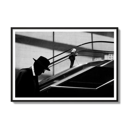 Fine art black and white street photograph of a man ascending an escalator. Archival pigment print, gallery size, black frame.