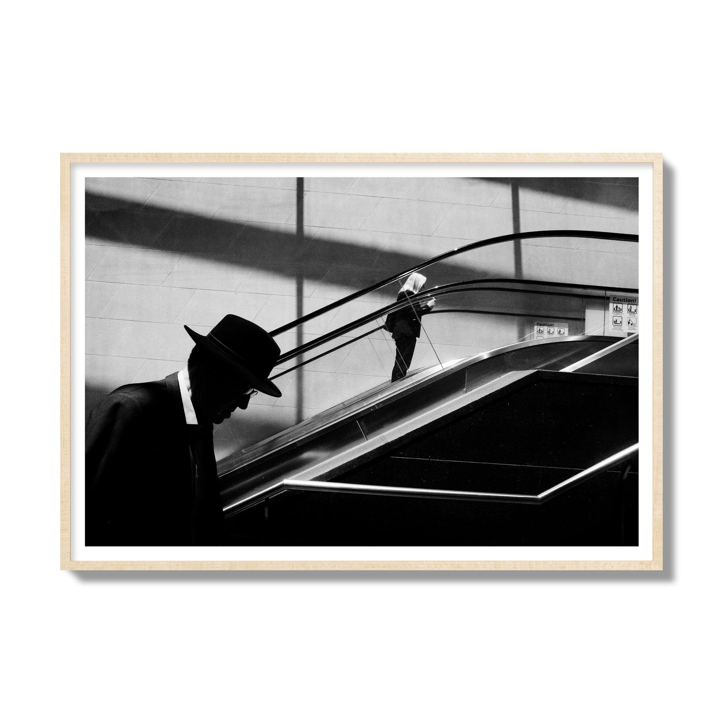 Fine art black and white street photograph of a man ascending an escalator. Archival pigment print, gallery size, natural wood frame.