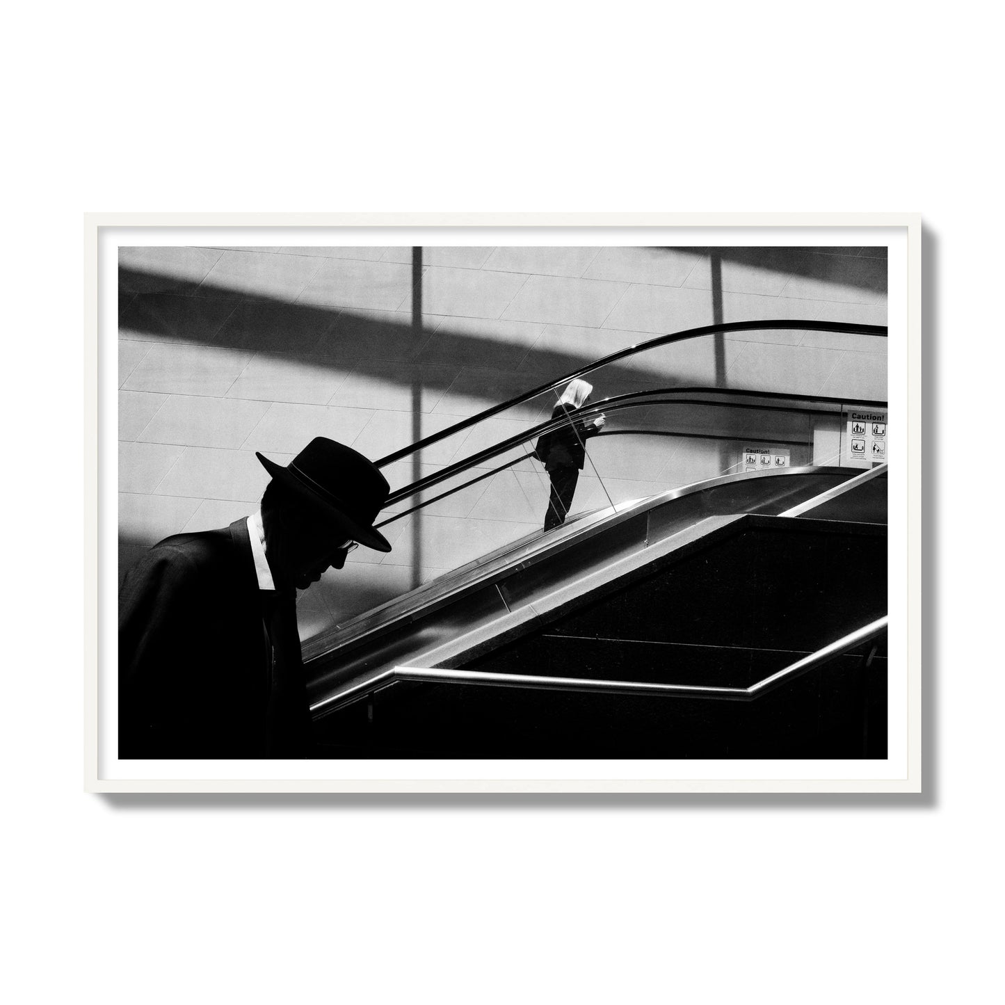 Fine art black and white street photograph of a man ascending an escalator. Archival pigment print, gallery size, white frame.