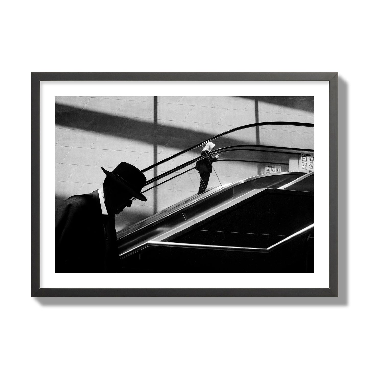 Fine art black and white street photograph of a man ascending an escalator. Archival pigment print, giant size, black frame.