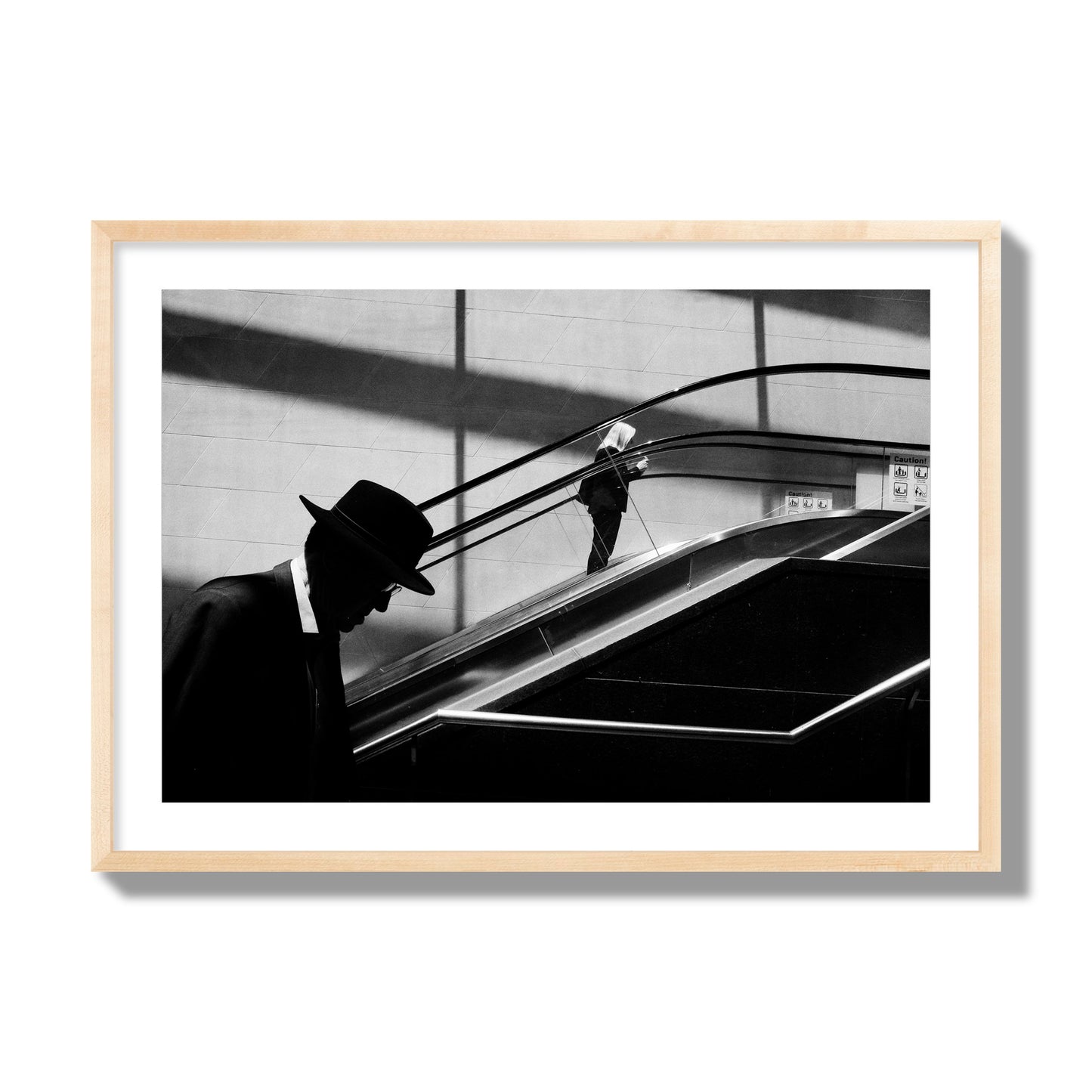 Fine art black and white street photograph of a man ascending an escalator. Archival pigment print, giant size, natural wood frame.
