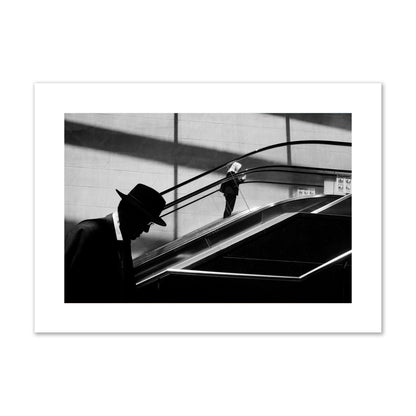 Fine art black and white street photograph of a man ascending an escalator. Archival pigment print, giant size, print.