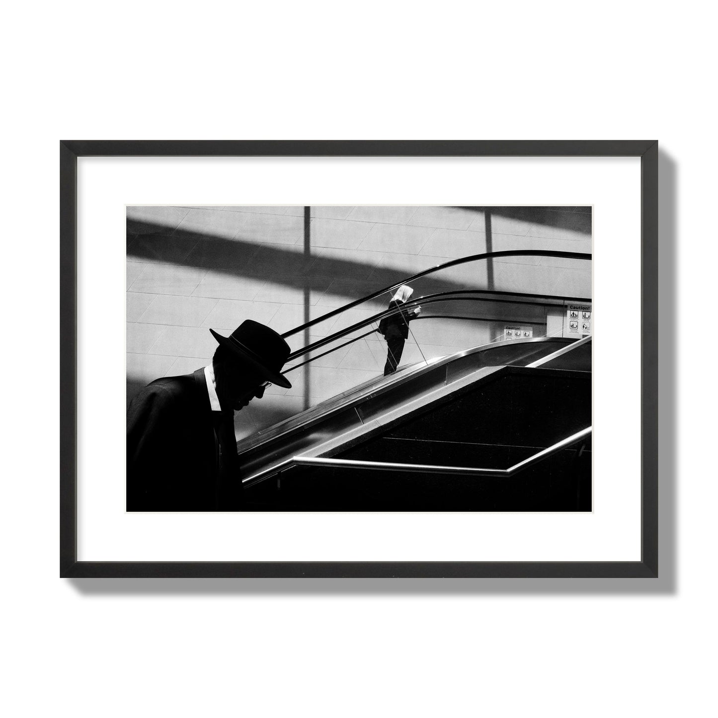 Fine art black and white street photograph of a man ascending an escalator. Archival pigment print, large size, black frame.